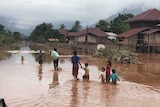 Seven people, five of them children, wade through a village street flooded with muddy water
