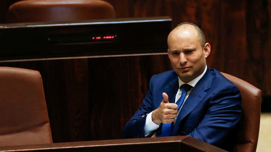 Naftali Bennett sitting in a blue suit gives a thumbs up sign.