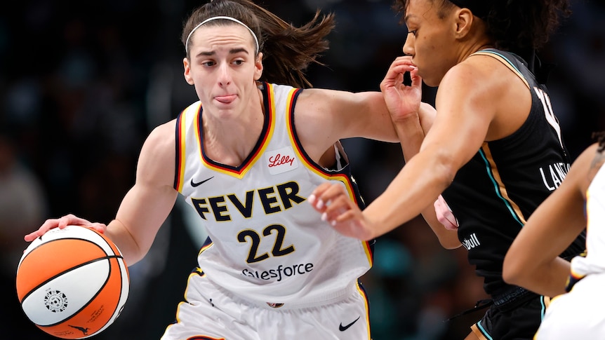 A woman in a white jersey with the words Fever and number 22 pushes a woman in a black jersey away