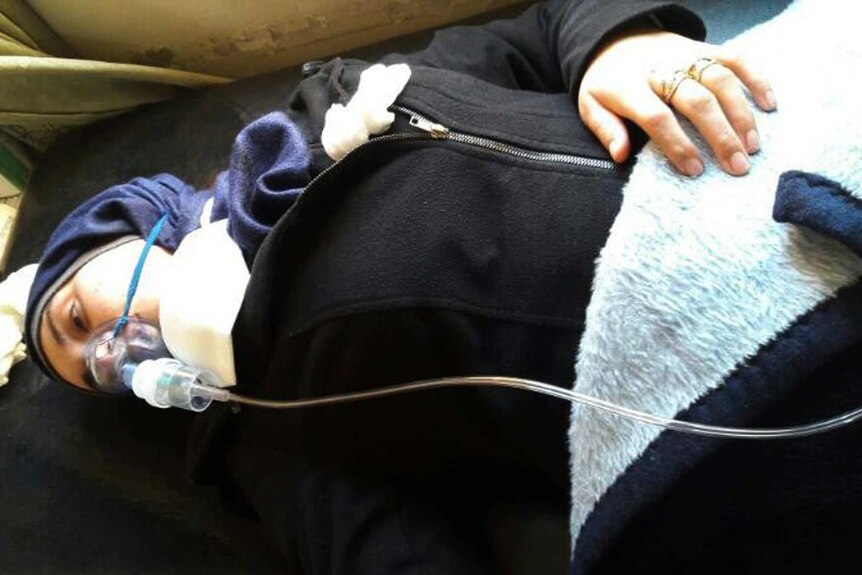Aya Fadl lies on a bed in Syria with an oxygen mask to heal breathing difficulties