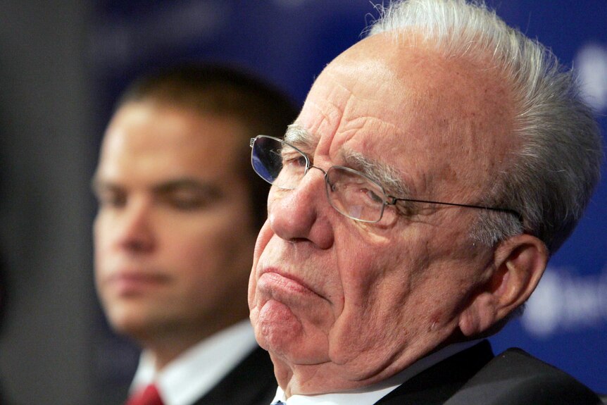Rupert Murdoch, frowning and wearing glasses, with Lachlan blurred in the backgorund