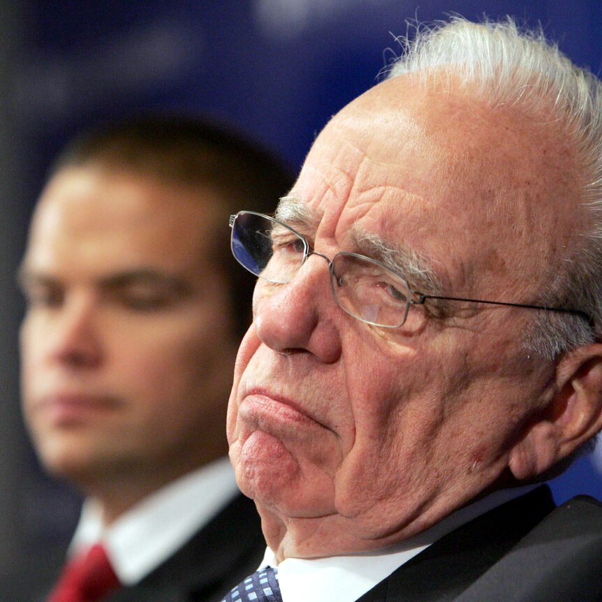 Rupert Murdoch, frowning and wearing glasses, with Lachlan blurred in the backgorund