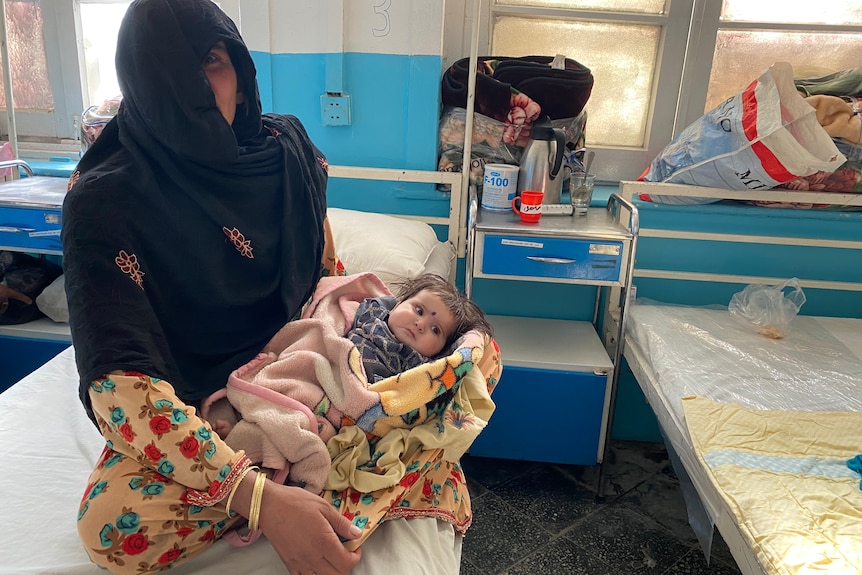 A woman in a black headscarf cradles a young baby on a hospital bed
