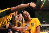 A woman in a yellow soccer shirt poses for a selfie with a young supporter. 