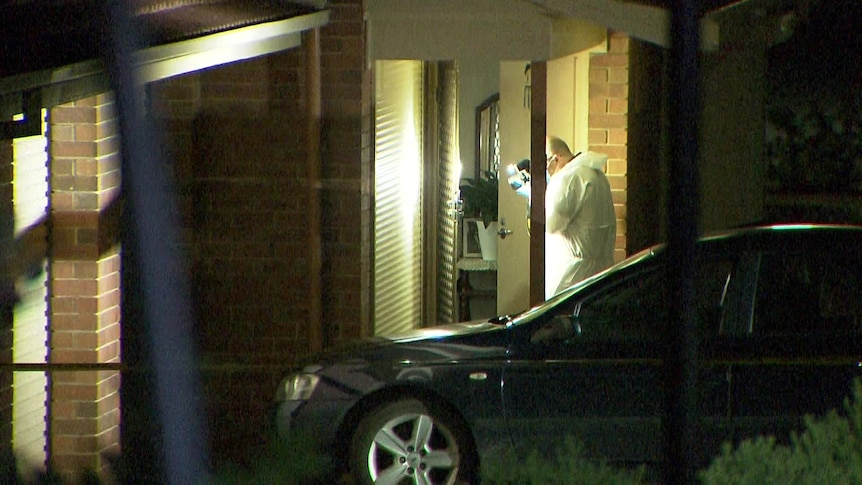 A man in crime scene white uniform taking photographs of a door next to a car