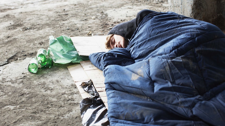 Homeless man sleeping in sleeping bag on cardboard