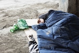 Homeless man sleeping in sleeping bag on cardboard