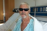 A man in sunglasses rests on a bed.