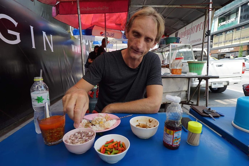 Man eats street food at a stall on a Bankok side walk