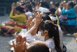 A row of Balinese women in face masks praying