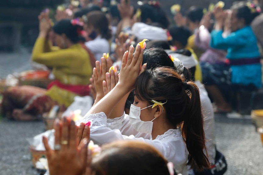 A row of Balinese women in face masks praying