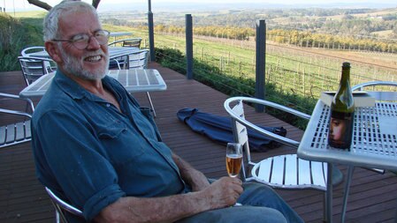 Borry Gartrell sits on his deck drinking a glass of wine and smiling.