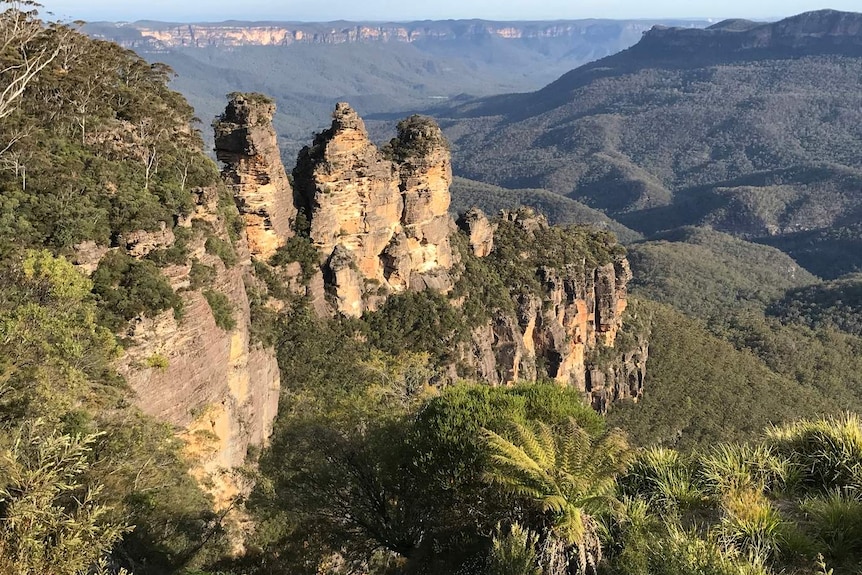 a rock formation with three prongs in rolling green mountain ranges