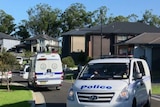 Police vehicles and police tape block off a street full of large two-storey houses.