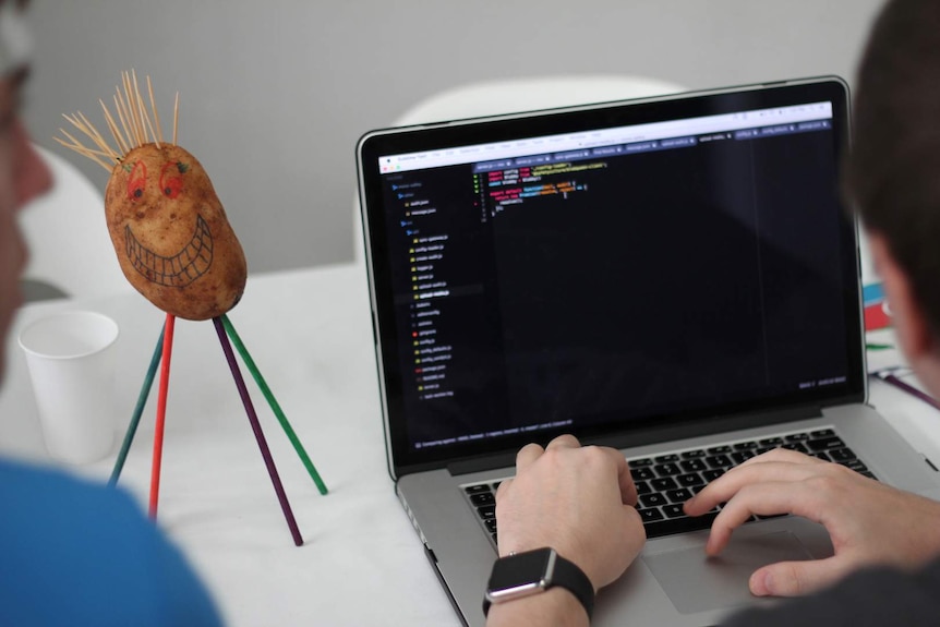 A potato with a face drawn on sits next to a laptop computer