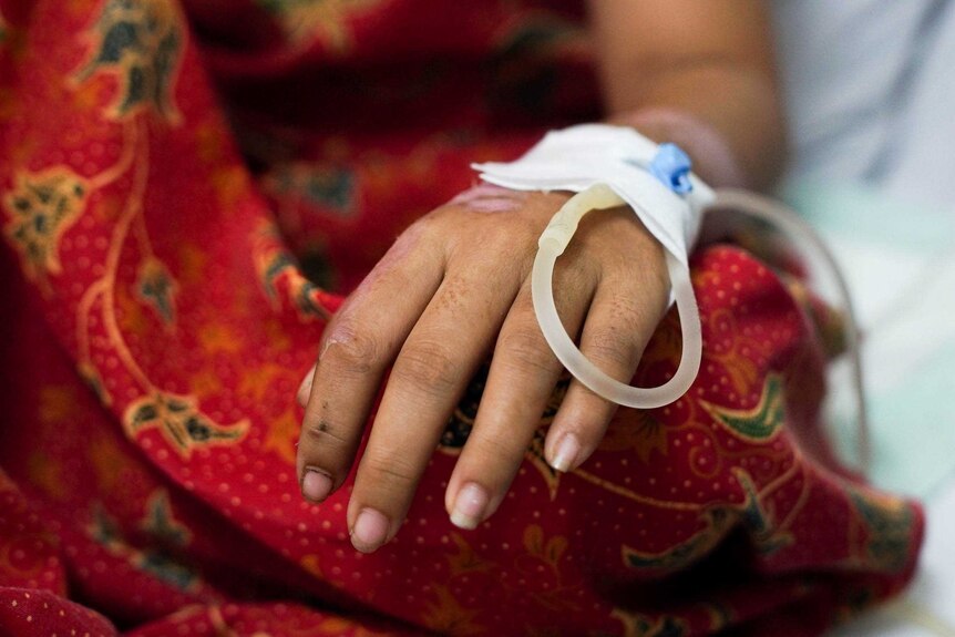 A hand with a drip attached to it rests in a red dress