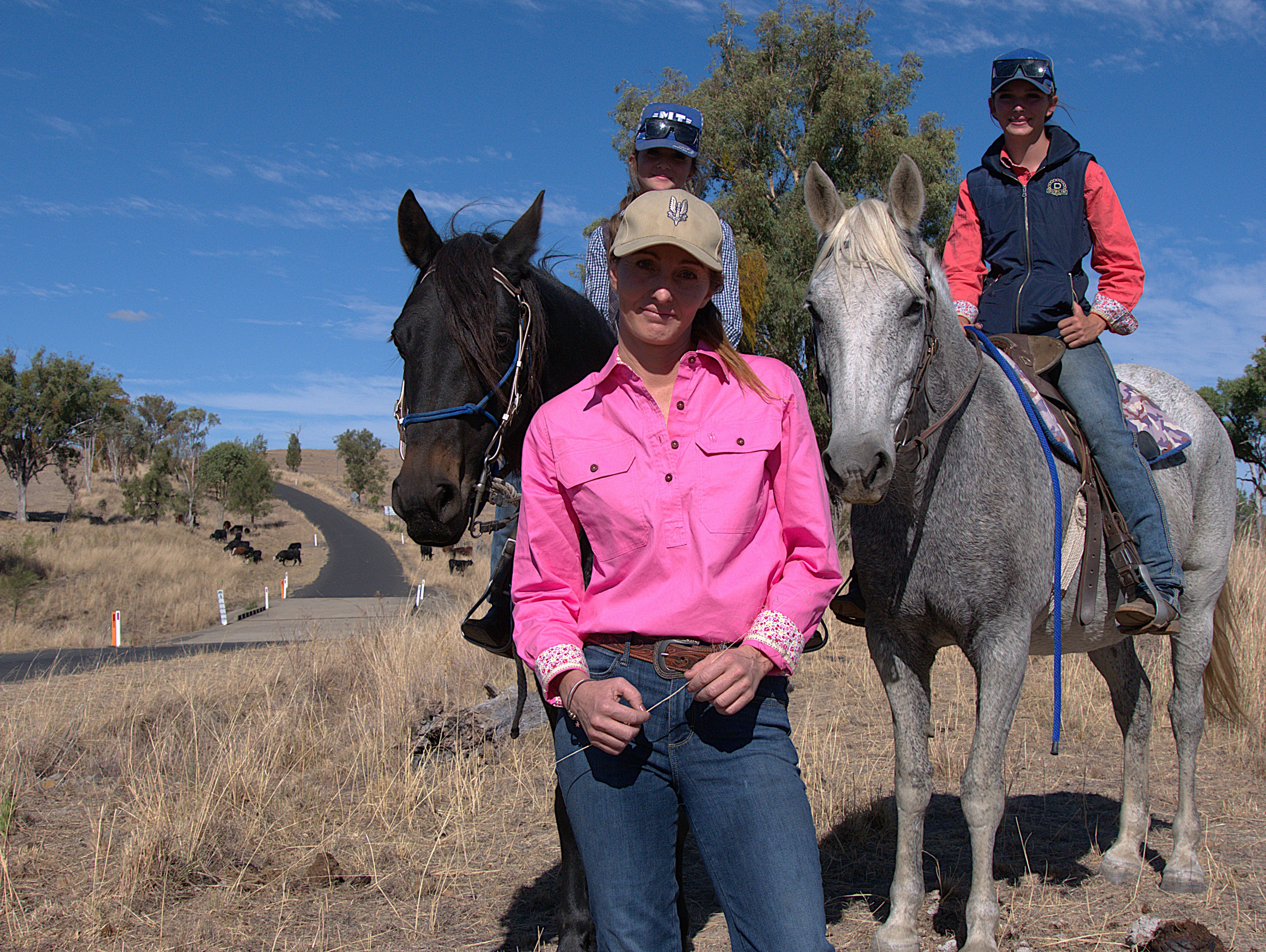 A woman in a pink shirt stands in front of two girls on horses.