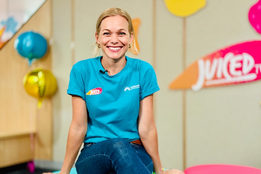 A woman in a blue t-shirt and jeans sits, smiling.
