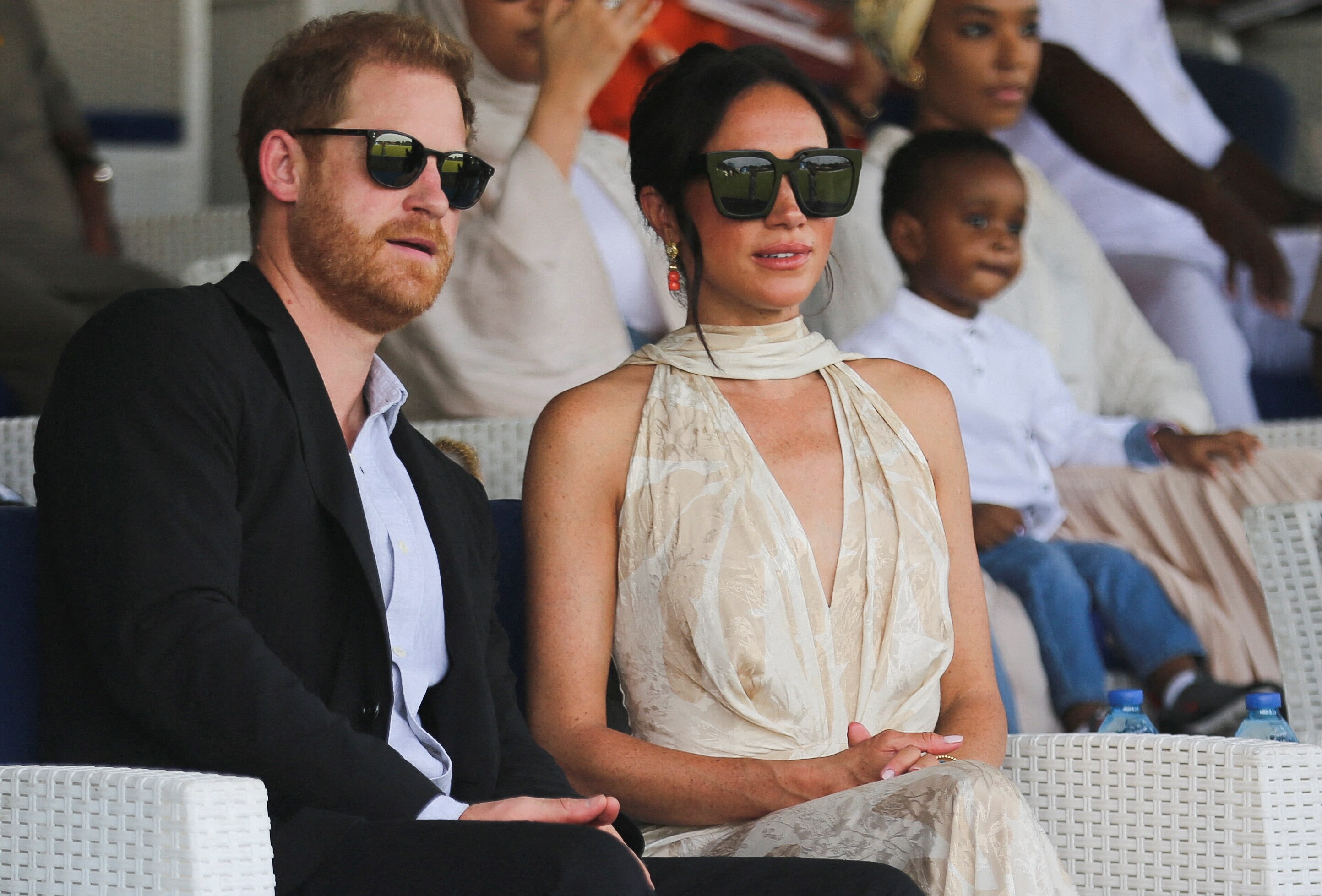 A man and a woman in sunglasses sit in the stands of a stadium