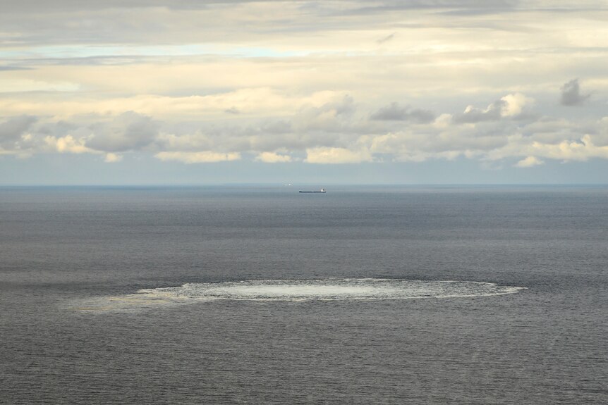 a circle o white water in the baltic sea with a cloudy sky and a ship in the background