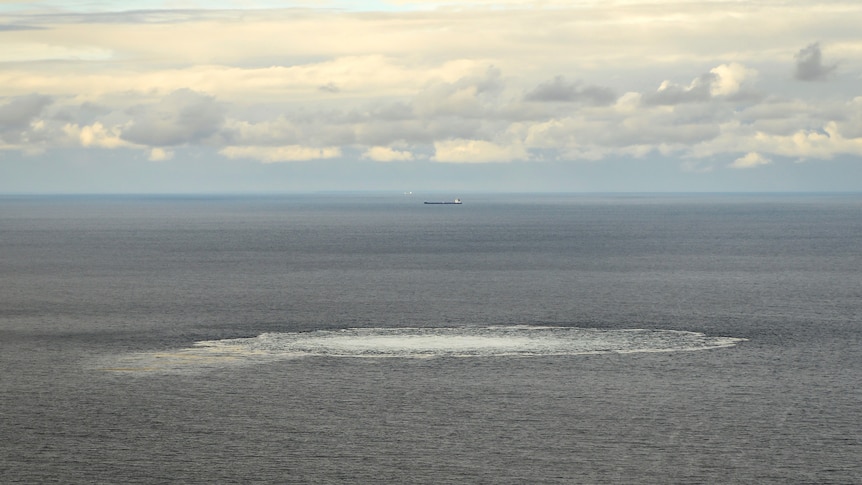 a circle o white water in the baltic sea with a cloudy sky and a ship in the background