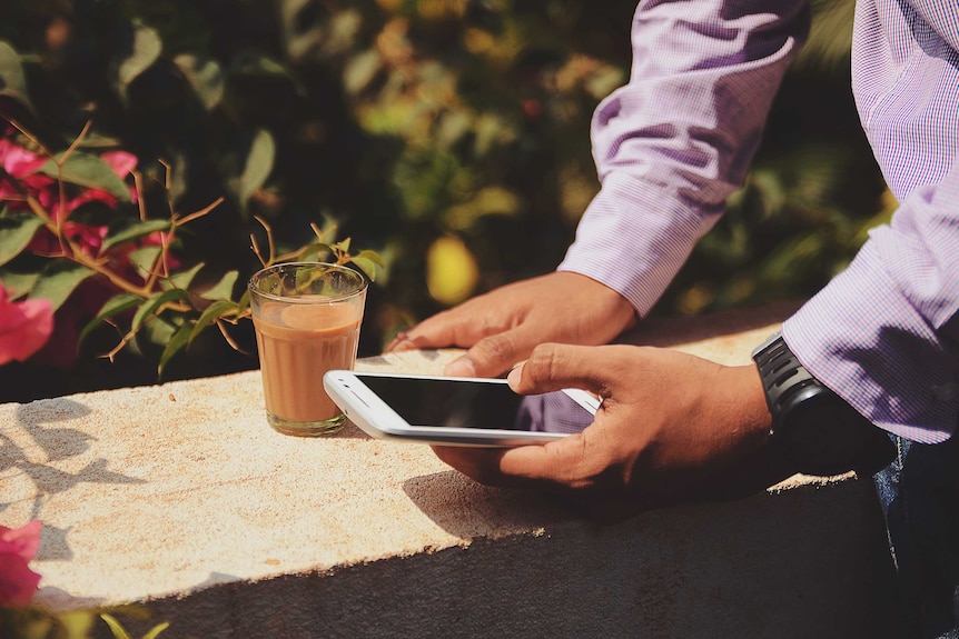 Man holding phone next to glass of coffee