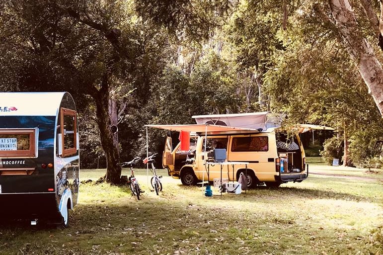 Yellow pop top campervan and little round caravan parked under trees