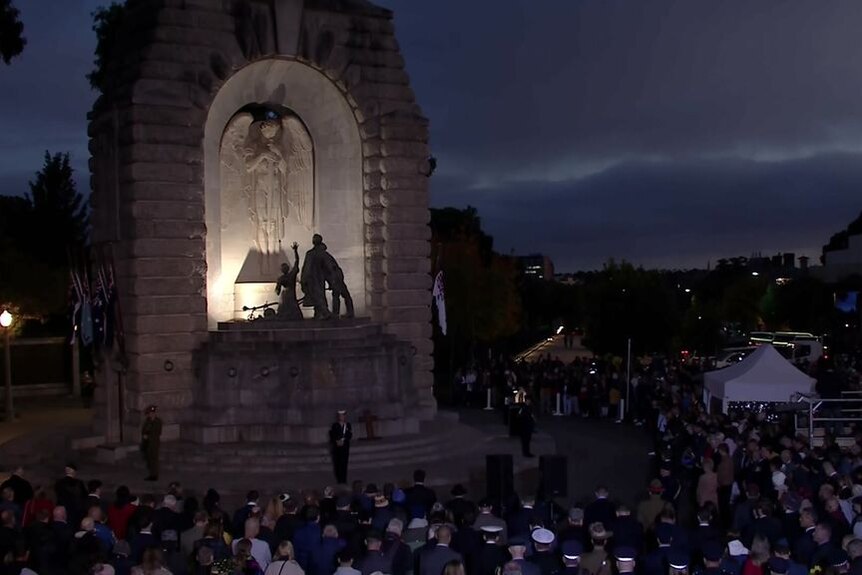 A crowd of people sit around the Adelaide National War Memorial at dawn