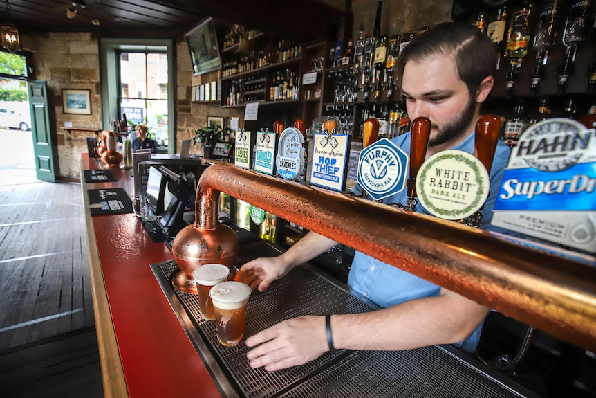 A barman pours beers from taps in an empty bar