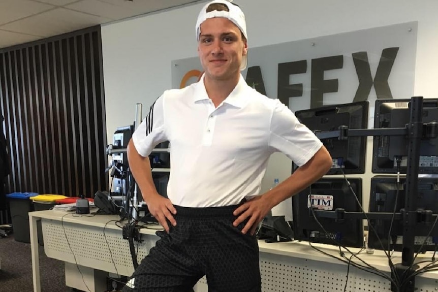 Deklan Gilmartin stands smiling with hands on hips wearing a baseball cap in an office.