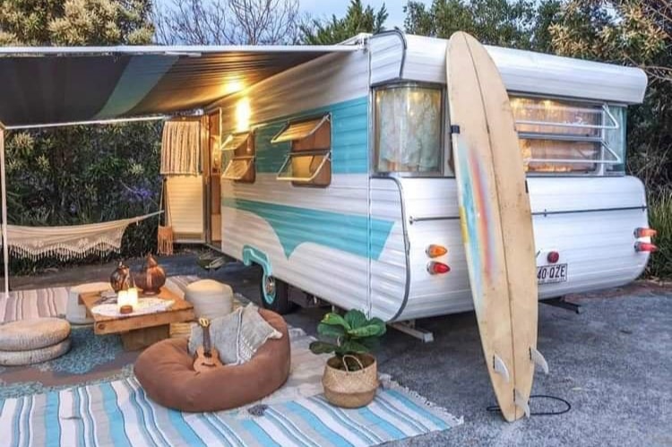 A retro caravan set up with surfboard, beanbags and hammock.