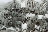 Black and white photo of a mena and women from Vanuatu with a white man standing behind them.