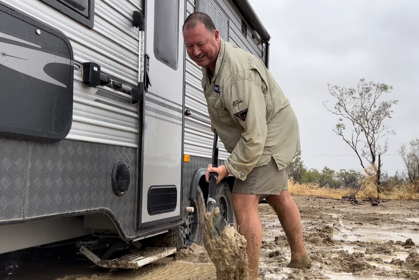 A man shovels mud around a stuck caravan