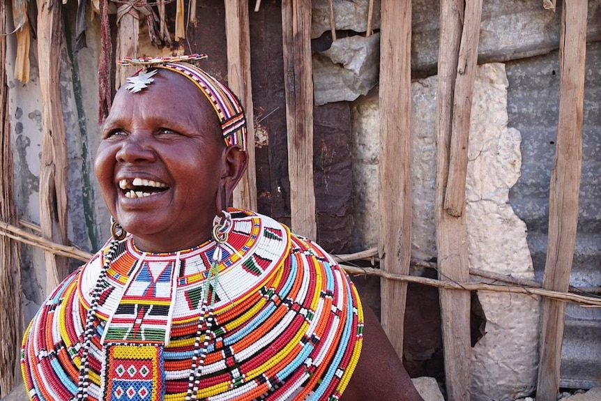 Mama Josephat smiles while wearing colourful beadwork around her neck and head.