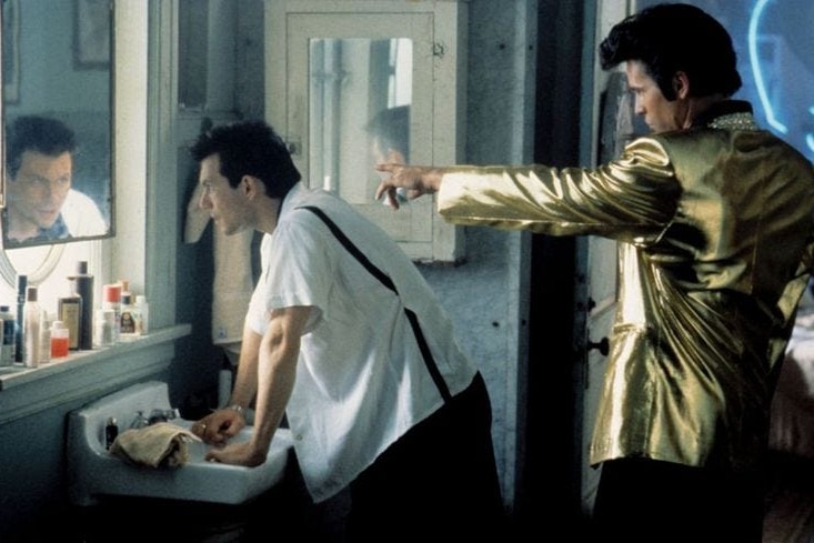 Val Kilmer points at Christian Slater from behind in Elvis attire, wile Slater looks at him from a bathroom mirror.
