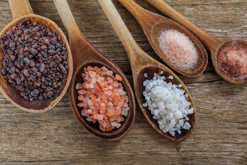 Five wooden spoons of varying size each containing a different type of salt.