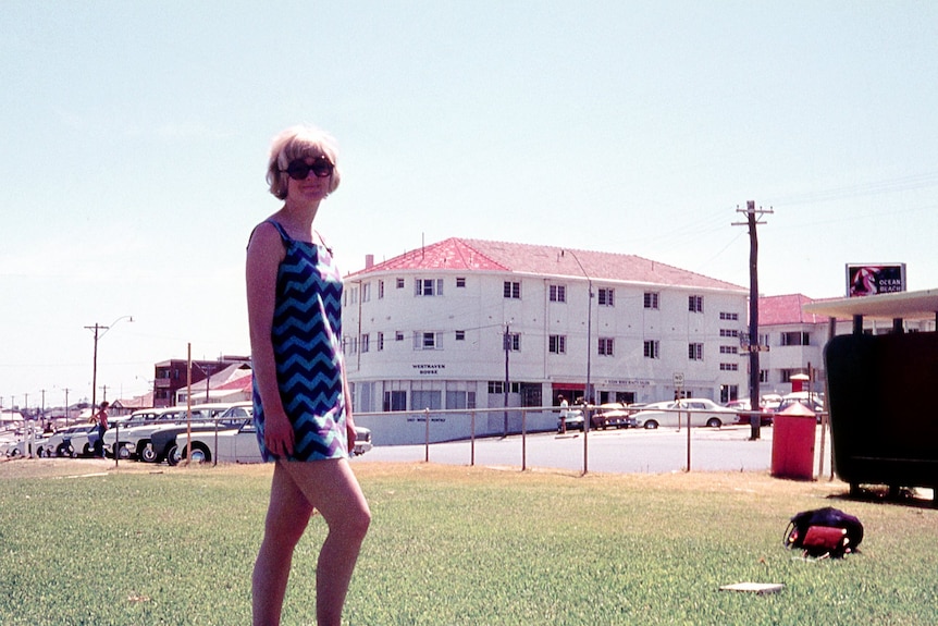 A woman in sunglasses and a dress with a white building in the background.