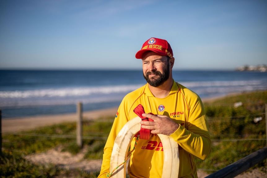 Patrick Jacob wearing the yellow and red surf lifesaving uniform and holding a rescue tube on the beach
