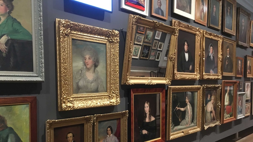 A gallery wall hung with many portraits, many in ornate gilt frames