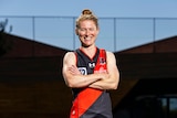 An Essendon Australian Rules footballer smiles at the camera in her team uniform.