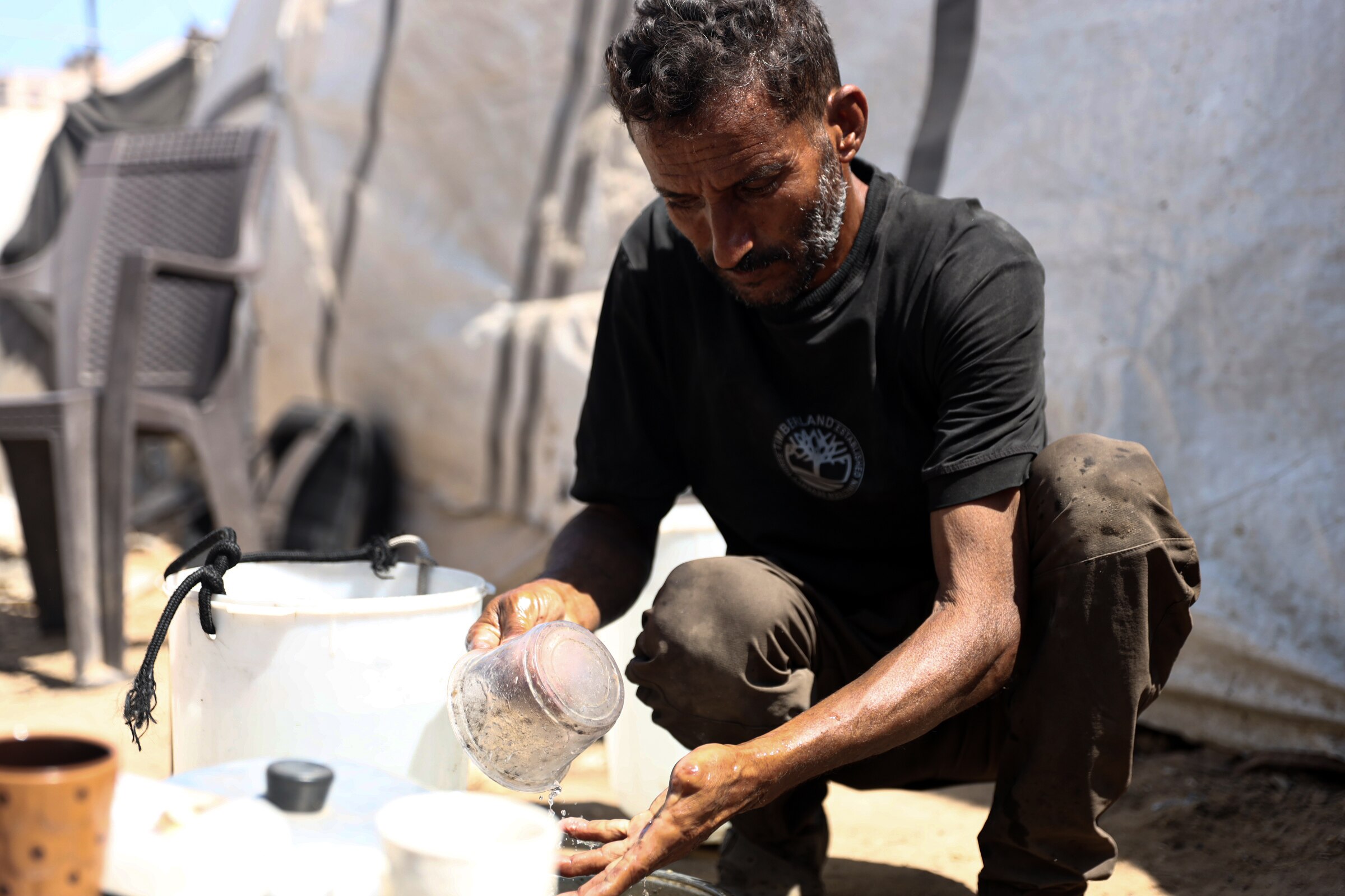 A man squats down as he pours water over his hands and into a bucket