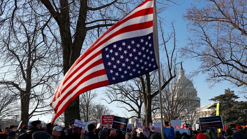 A US flag is raised over a crowd of people- the stars are in the bottom right corner, with the stripes above and to the left.