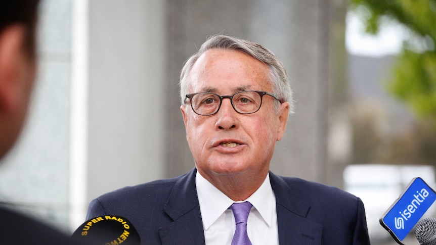 Wayne swan wears glasses and a blue tie speaking to reporters at a doorstop