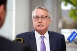 Wayne swan wears glasses and a blue tie speaking to reporters at a doorstop