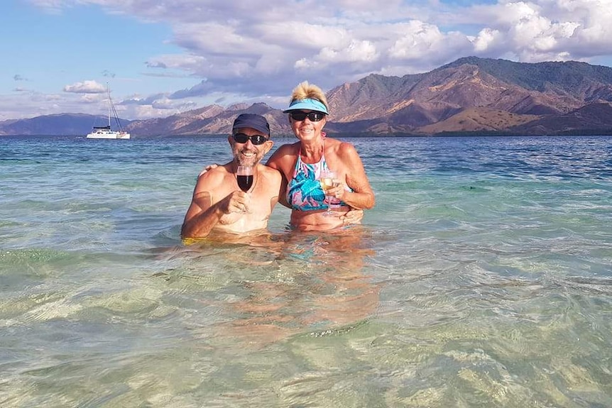 Craig and Del McEwan in clear blue water with a boat and mountains behind them.