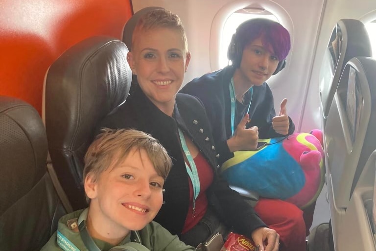 A mother smiling on plane with two adolescent children. 