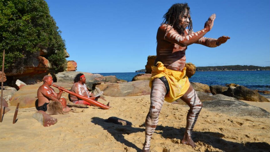 A man performs an Aboriginal war dance on the beach