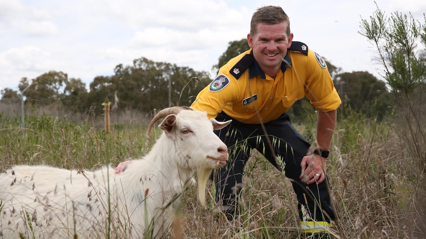 man smiling at camera with goat in foreground