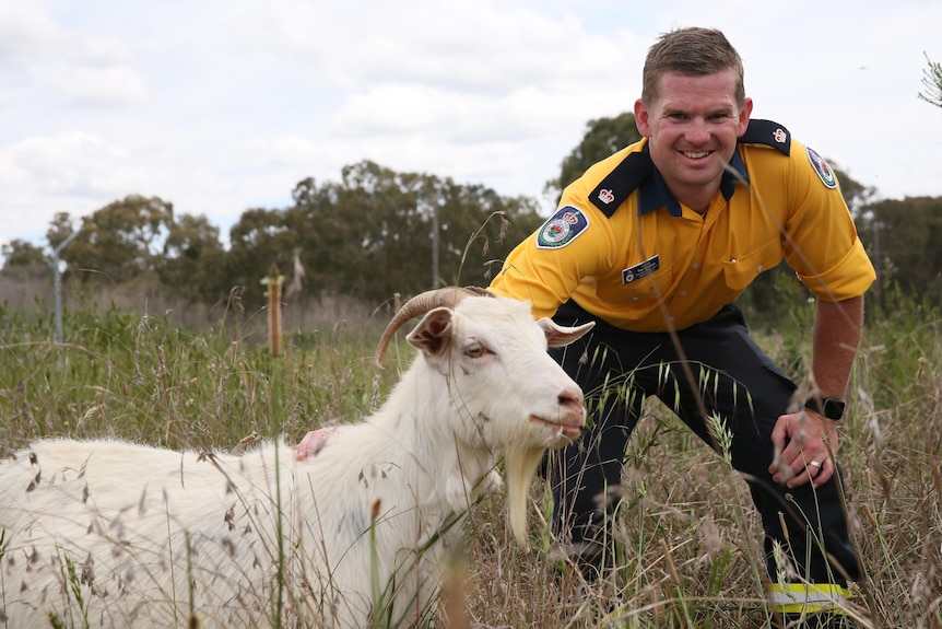 man smiling at camera with goat in foreground