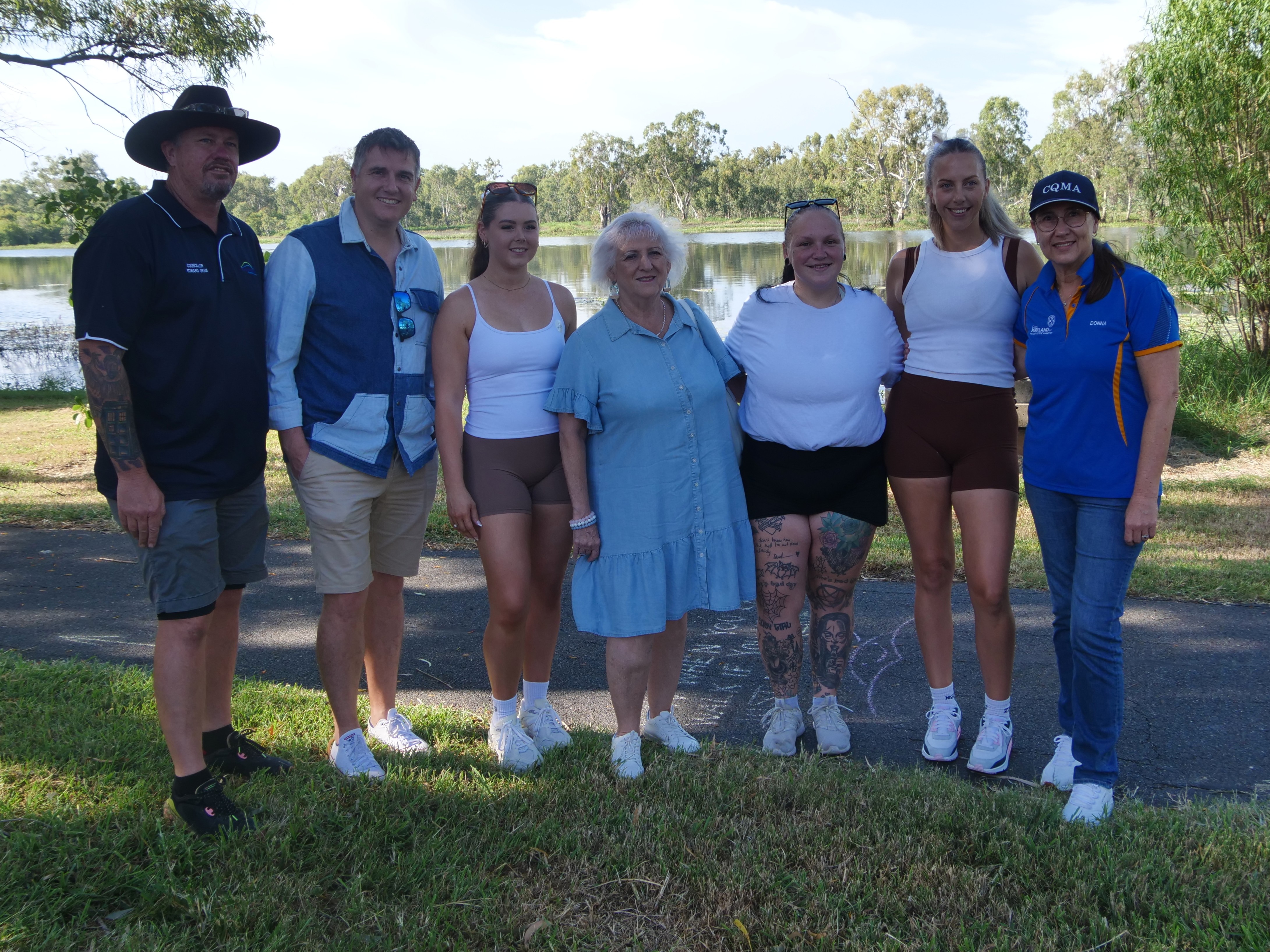 Grupo de mujeres en ropa deportiva y políticos masculinos y femeninos sonriendo a la cámara en el fondo de la laguna